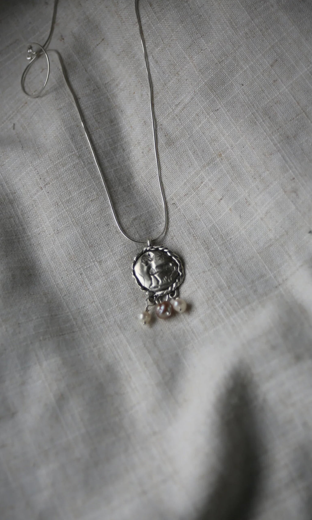 Plümo- Pearled Necklace: Sterling silver pendant with three freshwater pearls on a silver chain, displayed on gray textured fabric.