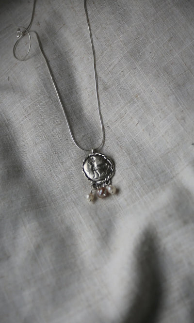 Plümo- Pearled Necklace: Sterling silver pendant with three freshwater pearls on a silver chain, displayed on gray textured fabric.