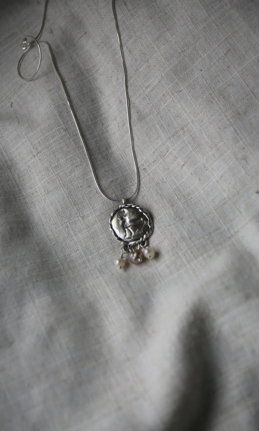 Plümo- Pearled Necklace: Sterling silver pendant with three freshwater pearls on a silver chain, displayed on gray textured fabric.