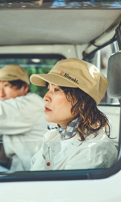 Plümo- Person in a Niwaki Cap with adjustable fit sits in a vehicle; another person is visible in the background.