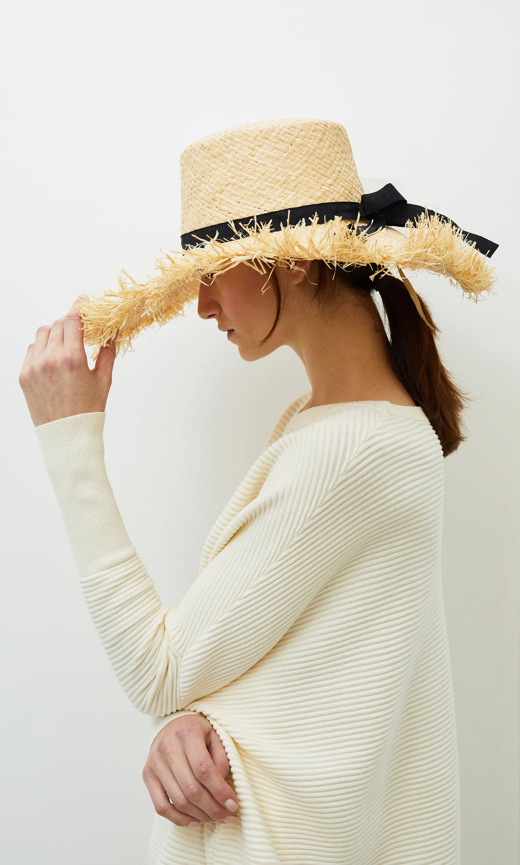 Plümo- Woman in a cream sweater and Frayed Straw Hat, facing sideways against a plain white background.