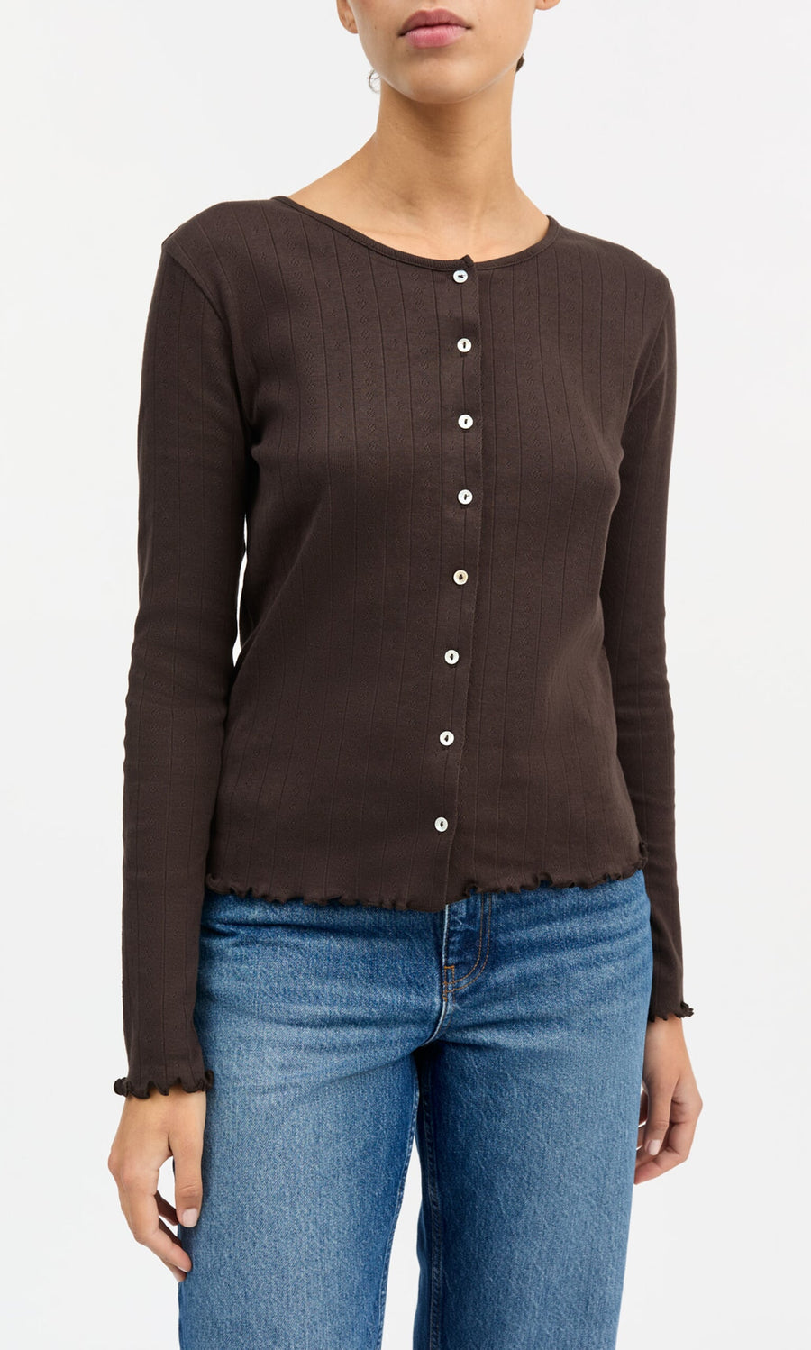 Plümo- Woman models the Eddie Cardigan—brown, long-sleeve, organic cotton—with blue jeans against a plain background.
