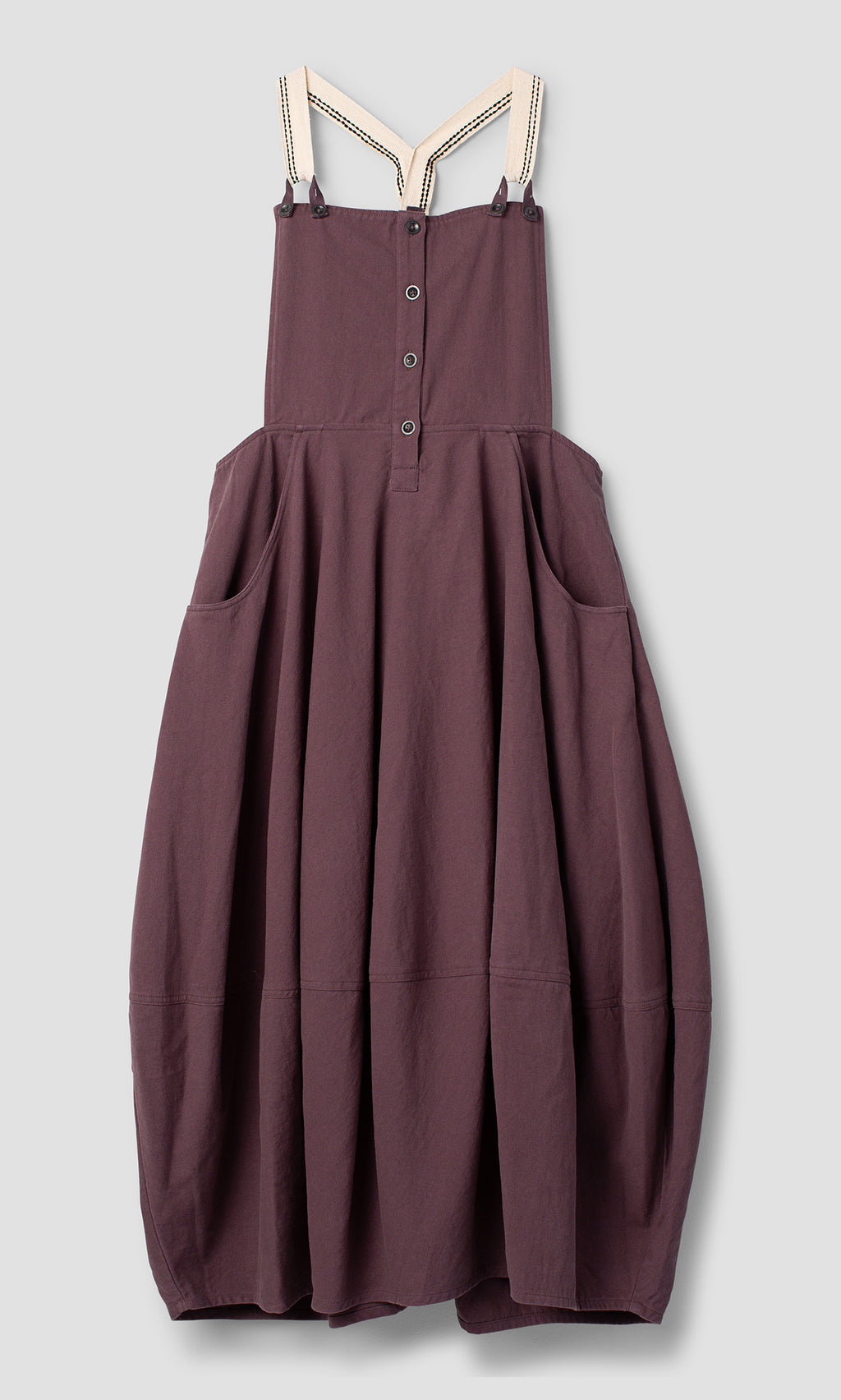 Plümo  Ingham Dungaree Dress in plum mulberry with a button-front bodice, side pockets, and striped shoulder straps.