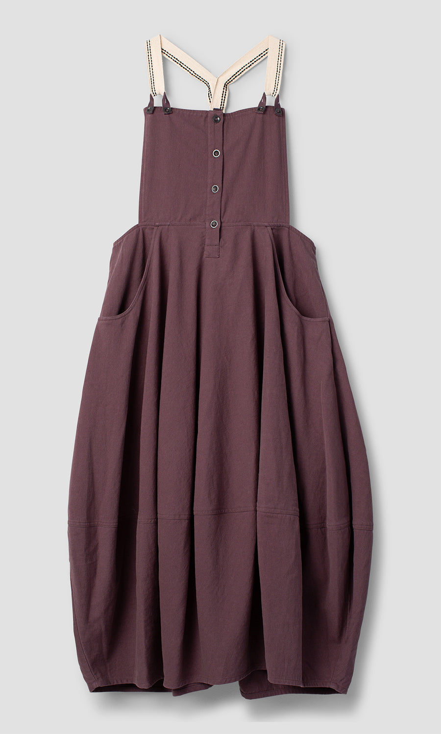 Plümo  Ingham Dungaree Dress in plum mulberry with a button-front bodice, side pockets, and striped shoulder straps.