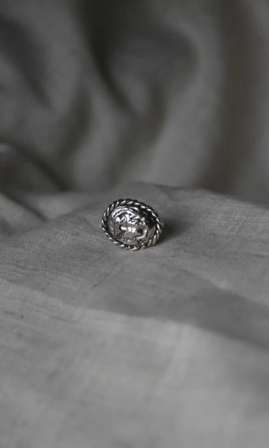 Plümo- The Silver Wild Ring, a handcrafted sterling silver piece with a sculpted face, rests on soft light gray fabric.