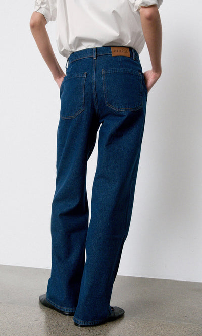Plümo- Person in a white shirt and Carlo Jeans stands with their back to the camera on a polished floor.