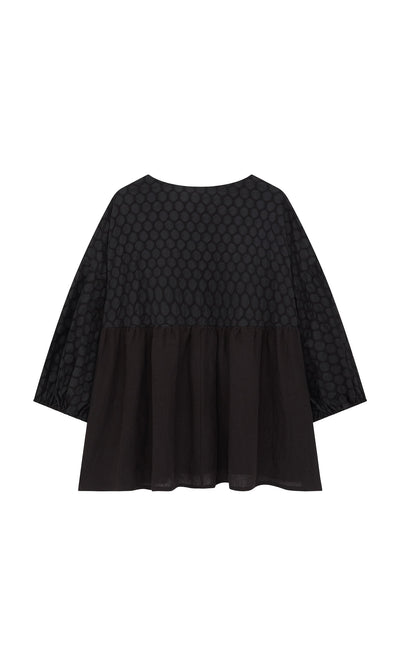 Plümo- The Tuppence Blouse is a loose black top with textured polka dots above a plain lower half, shown on white.