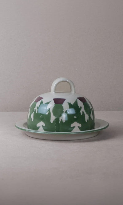 Plümo  Thistle Cheese Dome: Hand-painted ceramic with thistle design and handle, set on a plain background.