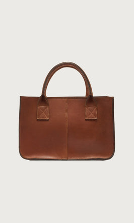 Plümo  A brown leather handbag with two short handles and visible stitching, set against a plain white background.