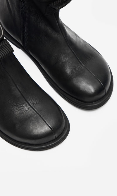 Plümo- Close-up of Ancona Boots in black waxy leather with round toes and visible stitching on a white background.