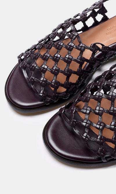 Plümo- Close-up of Arts Club Sandals—dark woven leather, handcrafted in Spain, open-toe with flat sole on a light background.