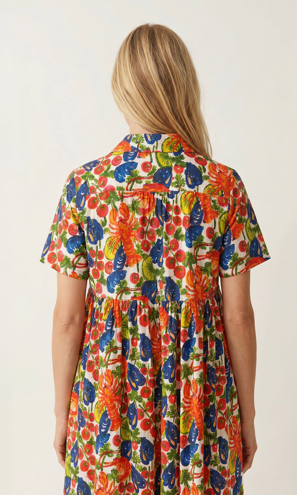 Plümo  Woman with long blonde hair in the vibrant, hand-printed cotton Astice Dress, seen from the back.