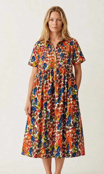 Plümo  Woman in the Astice Dress, a colorful, short-sleeve, hand-printed cotton voile, stands against a plain background.