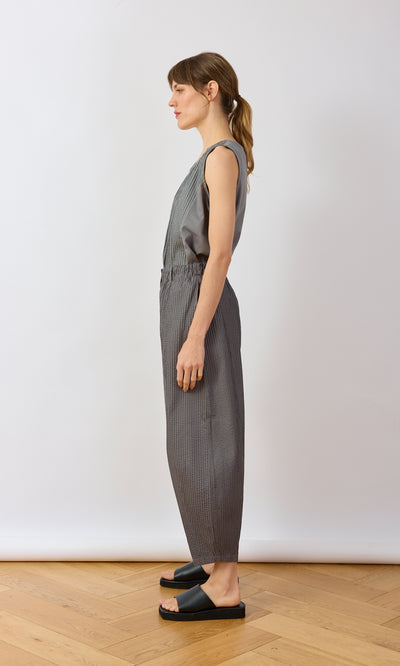 Plümo- Woman in profile wears a sleeveless gray top, Haru Grey Pants, and black slide sandals on a wooden floor.