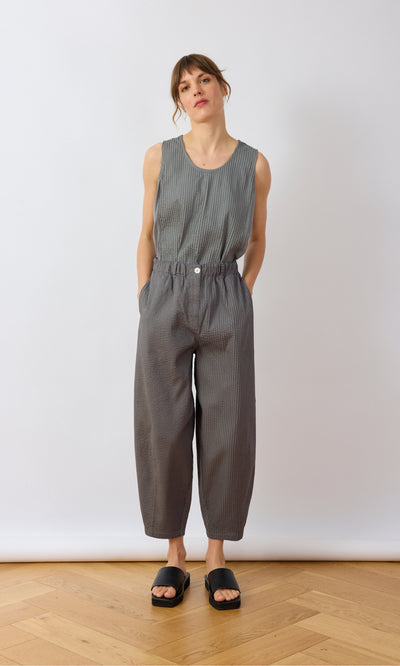 Plümo- Woman in a sleeveless gray top and Haru Grey Pants stands with hands in pockets against a white background.