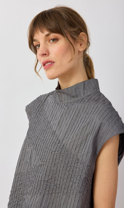 Plümo- Woman with light brown hair in a ponytail, wearing a gray Minato Top, looking slightly to the side.