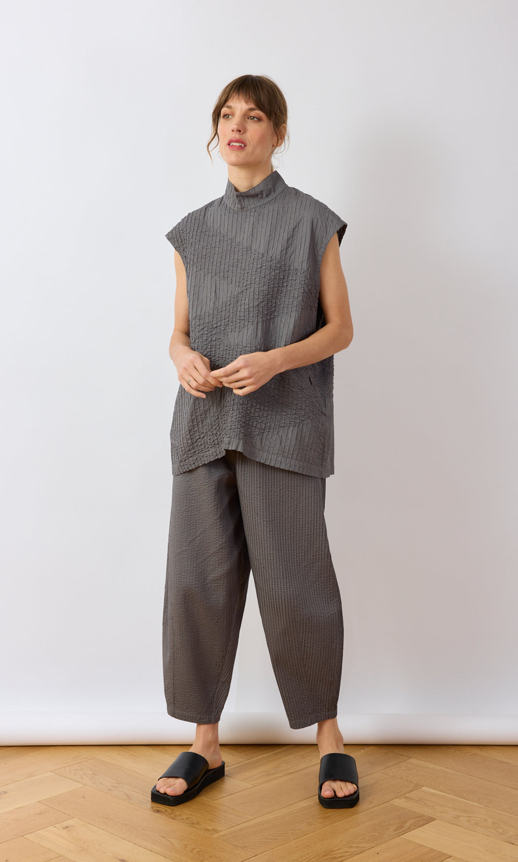 Plümo- Woman in a gray Minato Top and pants with black sandals, against a plain white background.