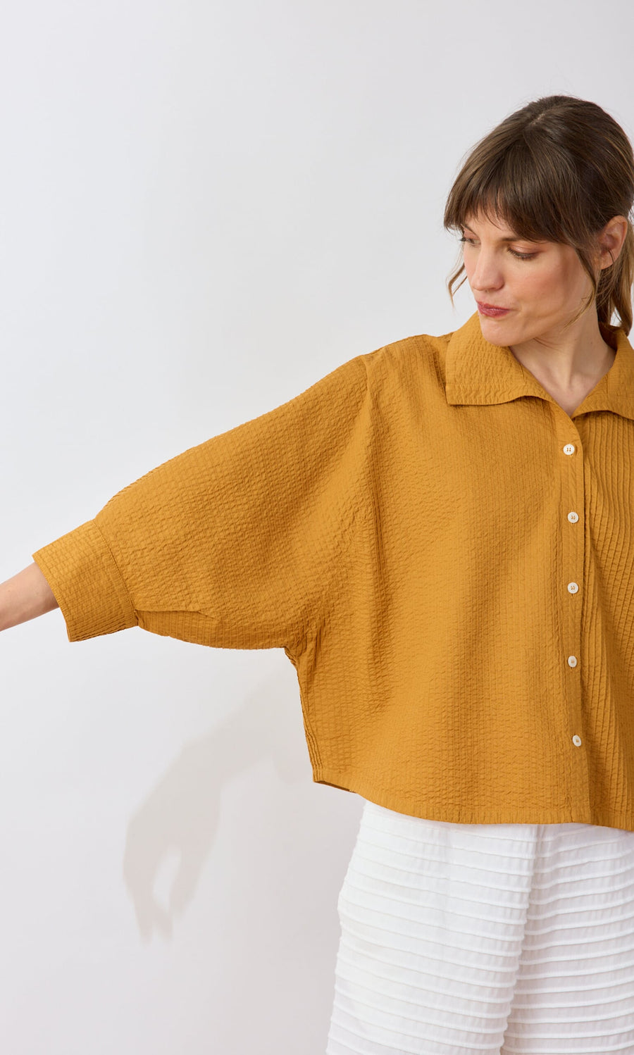 Plümo- Woman in the Karashi Shirt—loose mustard yellow with wide sleeves—paired with white textured pants.