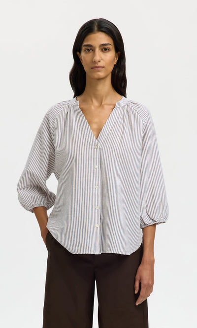 Plümo- A woman in a relaxed-fit Brisley Blouse with three-quarter sleeves and dark wide-leg pants stands against a plain background.