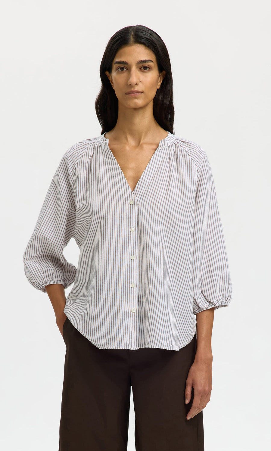 Plümo- A woman in a relaxed-fit Brisley Blouse with three-quarter sleeves and dark wide-leg pants stands against a plain background.