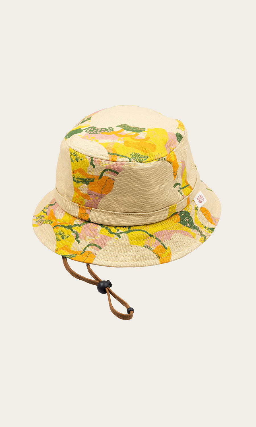 Plümo- Camo Bucket Hat: Beige canvas with yellow, green, and pink abstract pattern and an adjustable brown chin strap.