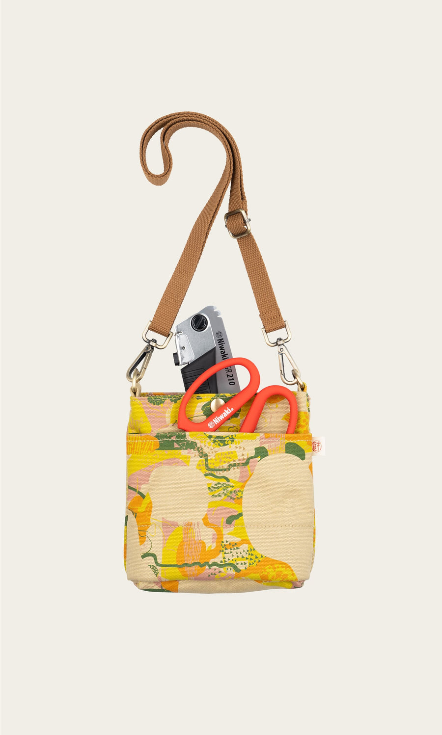 Plümo- Camo Pouch Bag fits a camera and red scissors, features a brown adjustable strap, shown on a light background.