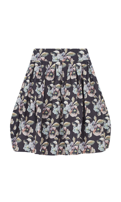 Plümo  The Pugh Flower Skirt is a short, pleated skirt with a dark base and an all-over delicate pastel floral pattern.