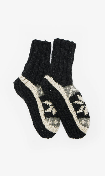 Plümo  Nordic Star Slipper Socks: hand-knitted wool, black cuffs and soles, gray and black geometric pattern on the foot.