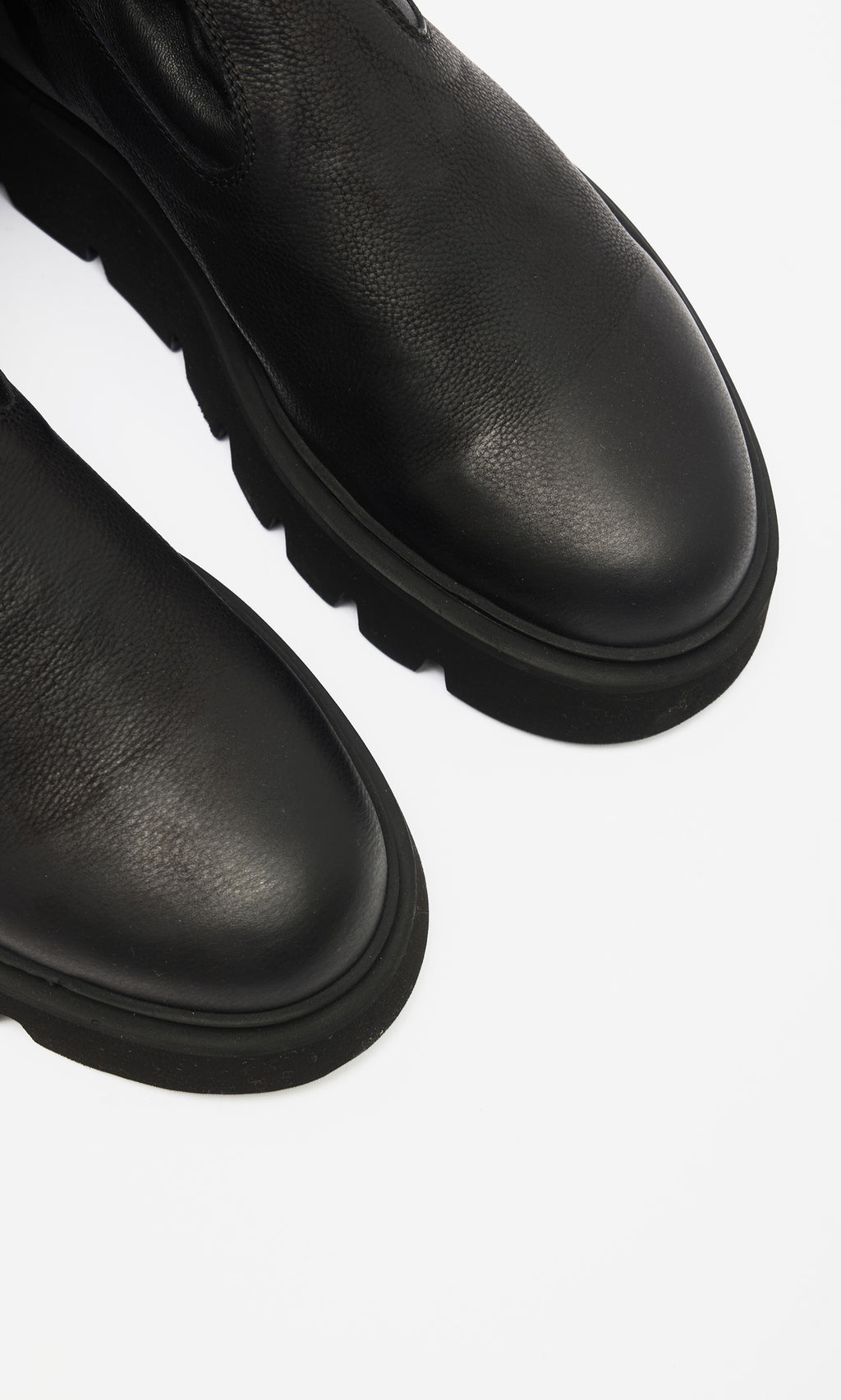 Plümo  Close-up of Long Prato Boots—black, knee-length with chunky ridged soles—shown on a white background.