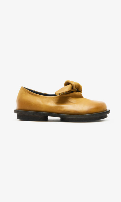 Plümo  Amber Leather Shoes in amber with bow and black sole, handcrafted; side view on white background.