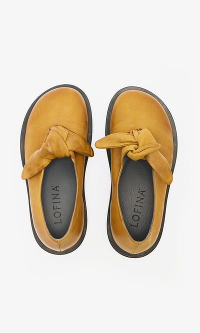 Plümo  Amber Leather Shoes: handcrafted tan leather shoes with knotted tops, black soles, top view on white background.