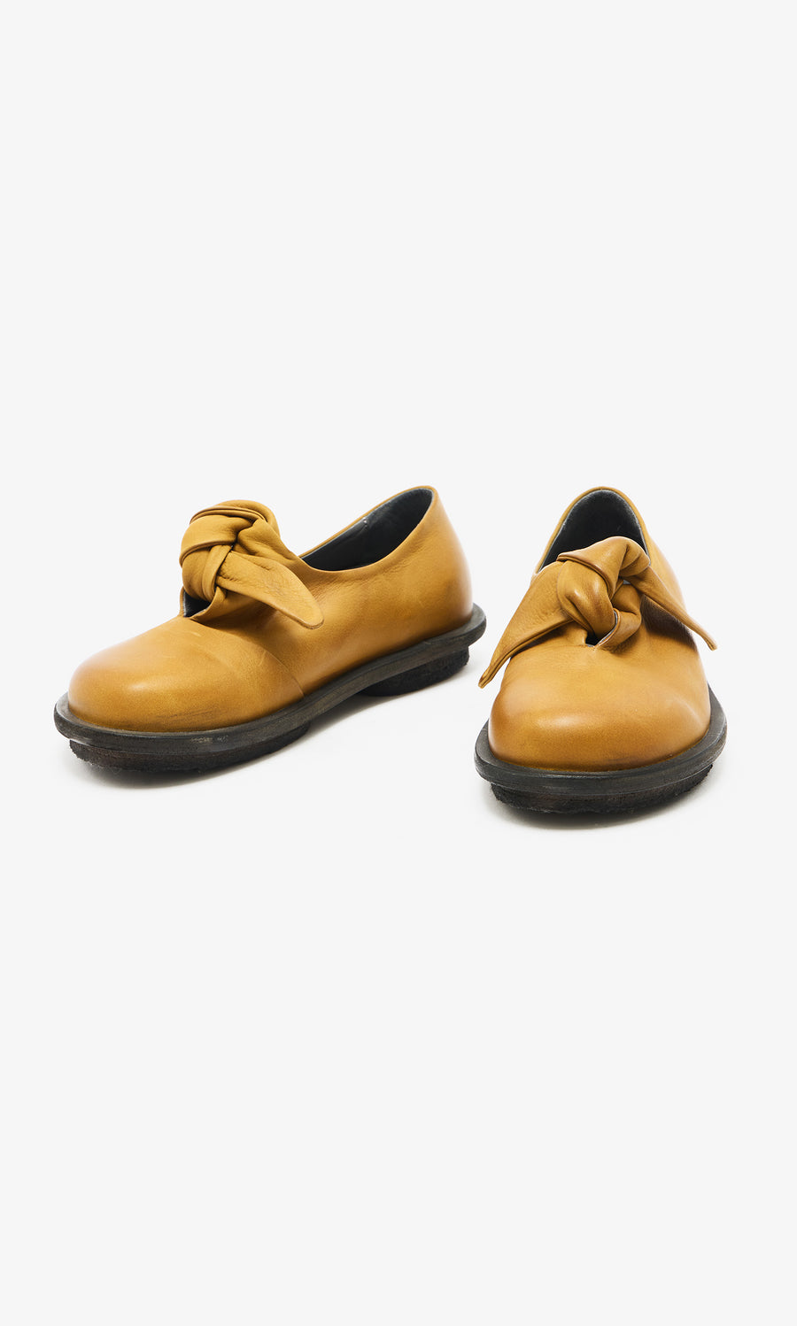 Plümo  Amber Leather Shoes: Mustard yellow flats with black soles, knotted bows, Danish-inspired, on white background.