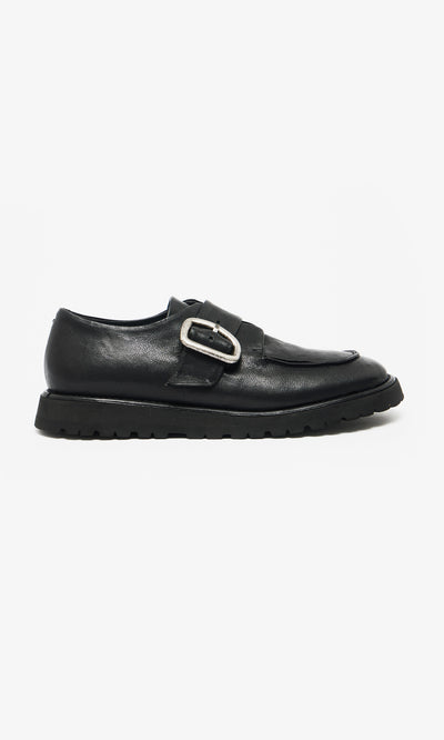 Plümo  Black Creepers feature black leather, a thick lugged rubber sole, and a large silver buckle on a white background.