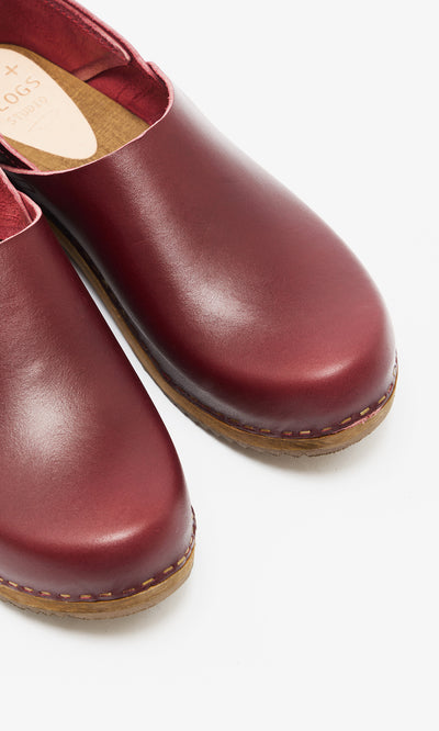 Plümo  A pair of Low Jord Clogs in burgundy leather with tan soles is displayed on a white background.