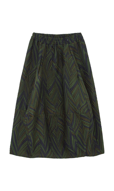 Plümo  The Yona Skirt features a green and navy leaf brocade, curved silhouette, and comfy elastic waistband.