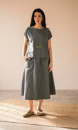 Woman wearing a gray outfit standing on a wooden floor with a beige wall background