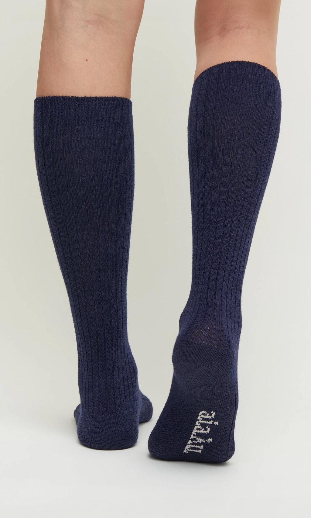 Plümo- Person wears Navy Cashmere Socks with white text on the bottom of one sock.