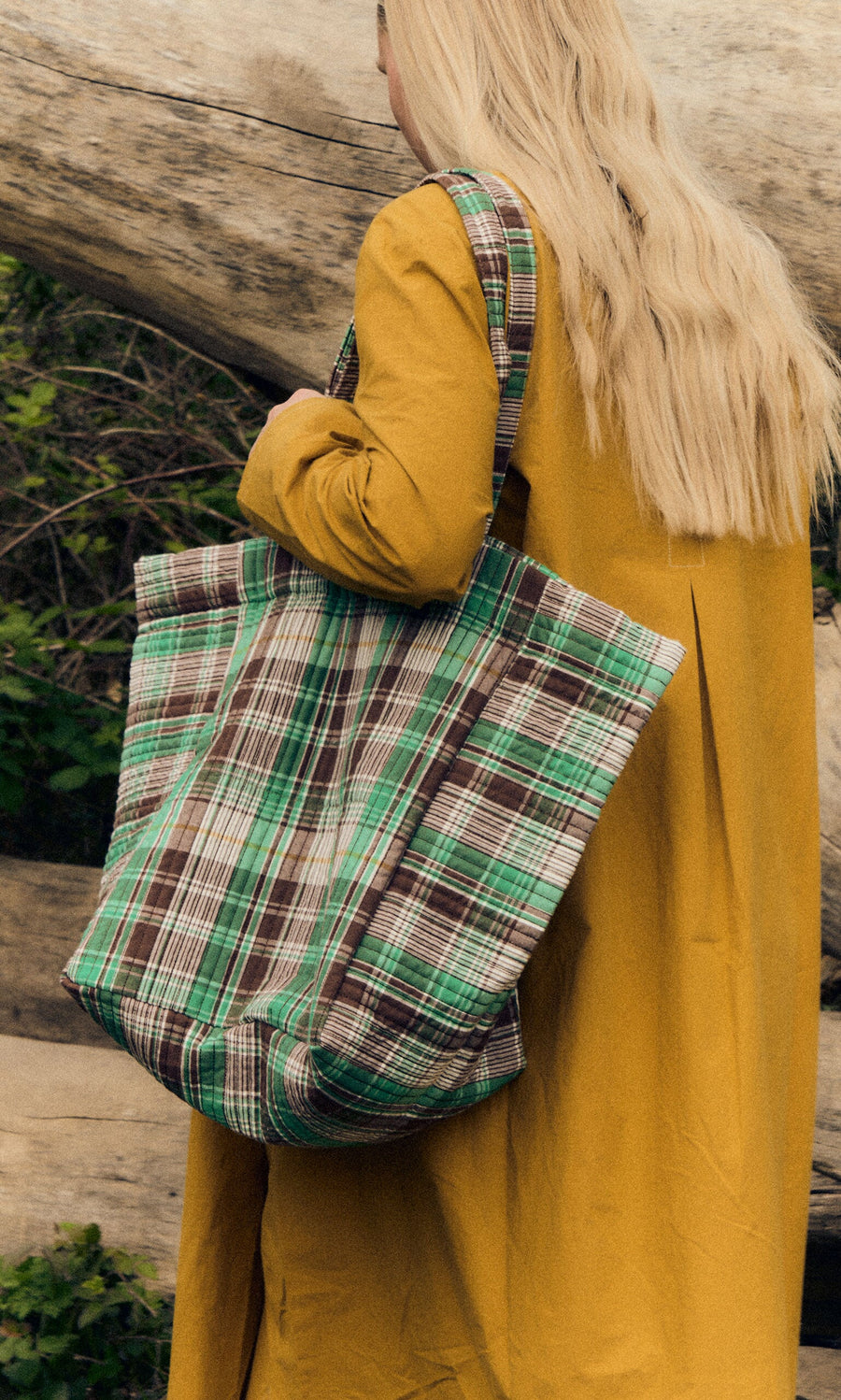 Plümo- Person with long blonde hair in a mustard coat carrying the Checked Quilted Bag outdoors.