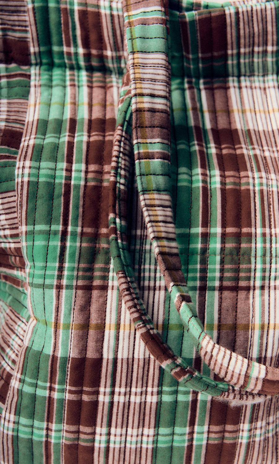 Plümo- Close-up of the Checked Quilted Bag, featuring green, brown, and white plaid with a curved fabric shoulder strap.