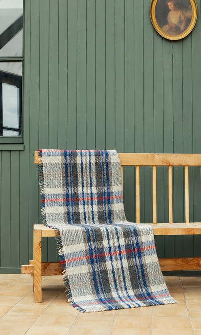 Plümo  A Random Throw with blue, red, and grey plaid stripes draped over a wooden bench.