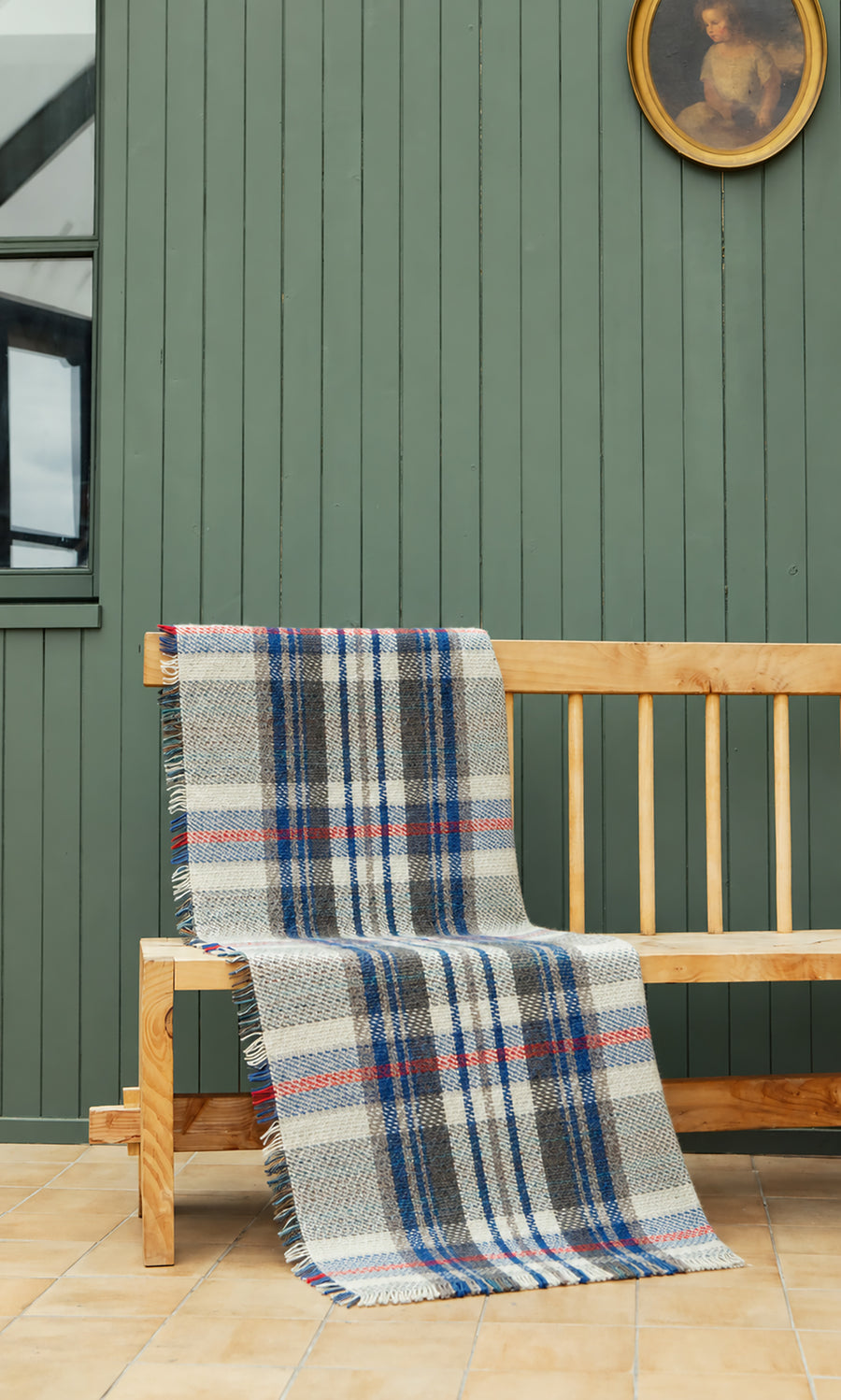 Plümo  A Random Throw with blue, red, and grey plaid stripes draped over a wooden bench.