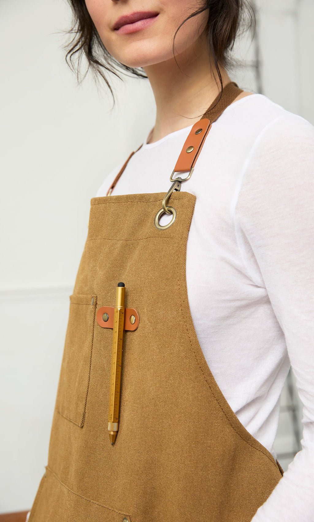 Plümo- Woman in a tan apron with a Workshop Pen in the front pocket, wearing a white long-sleeve shirt.