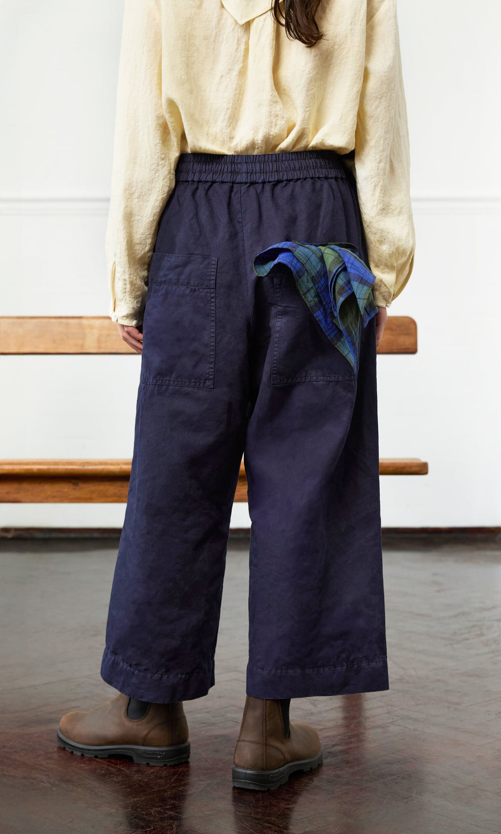Plümo- Person in Cromer Pants - Navy, cotton twill beige shirt, brown boots, plaid cloth in pocket, standing indoors.