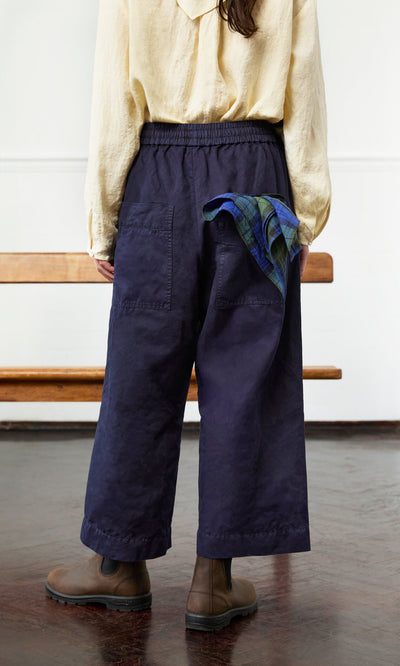 Plümo- Person in Cromer Pants - Navy, cotton twill beige shirt, brown boots, plaid cloth in pocket, standing indoors.