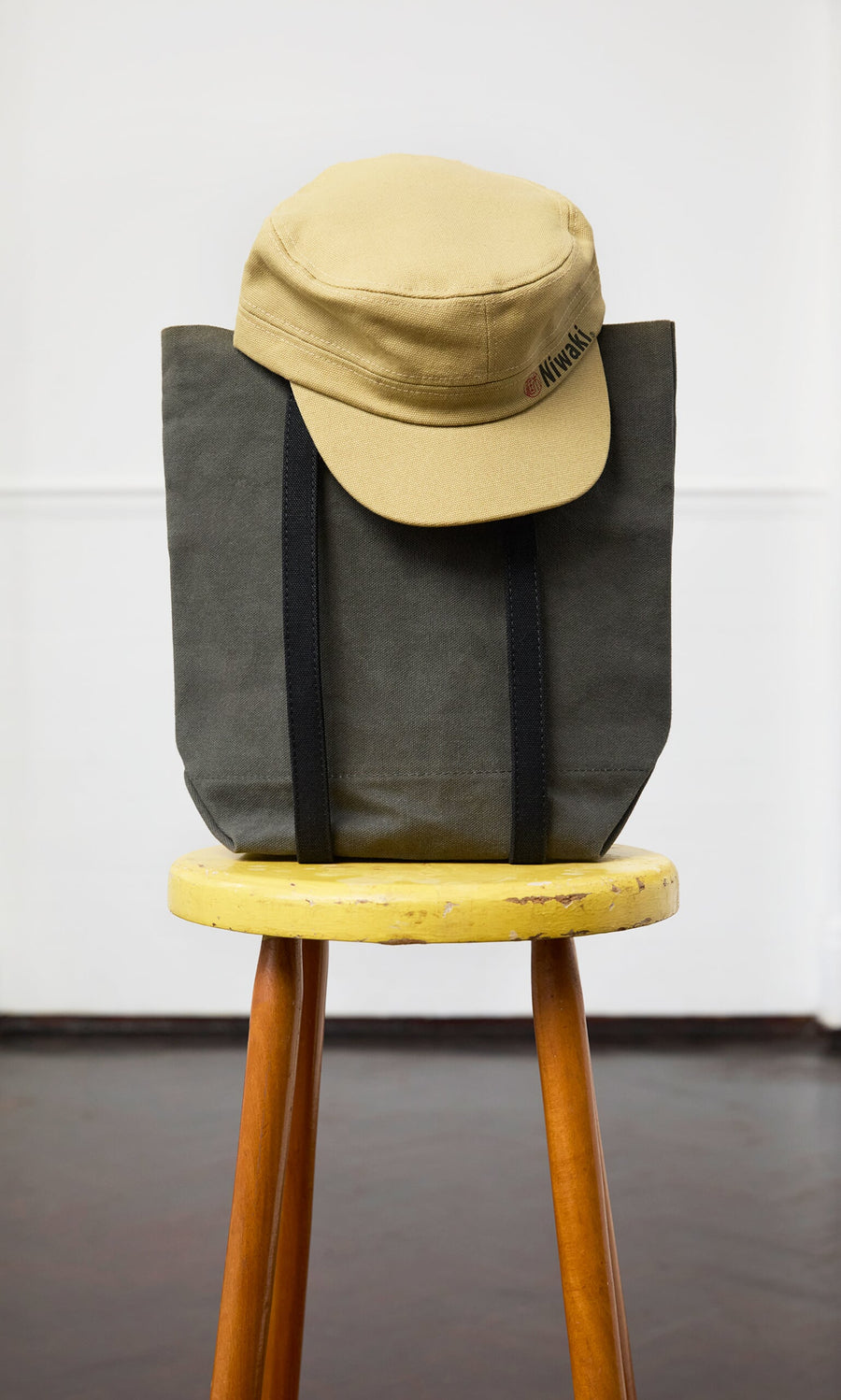 Plümo- A Niwaki Cap with an adjustable fit sits on a gray tote bag atop a yellow wooden stool.