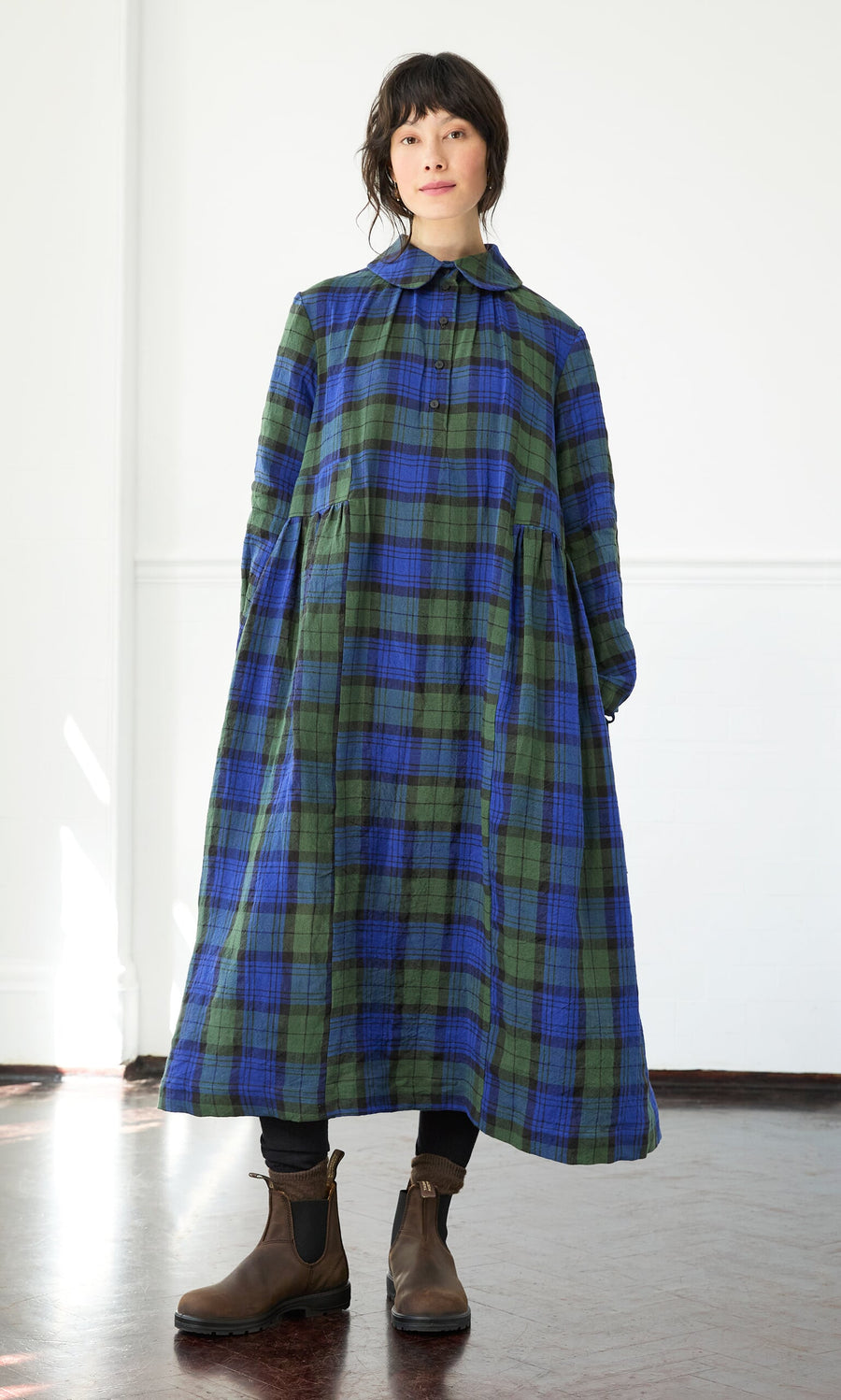 Plümo- Woman wears the Laois Tartan Dress—a loose, long-sleeved Irish linen dress with a Peter Pan collar and brown boots.