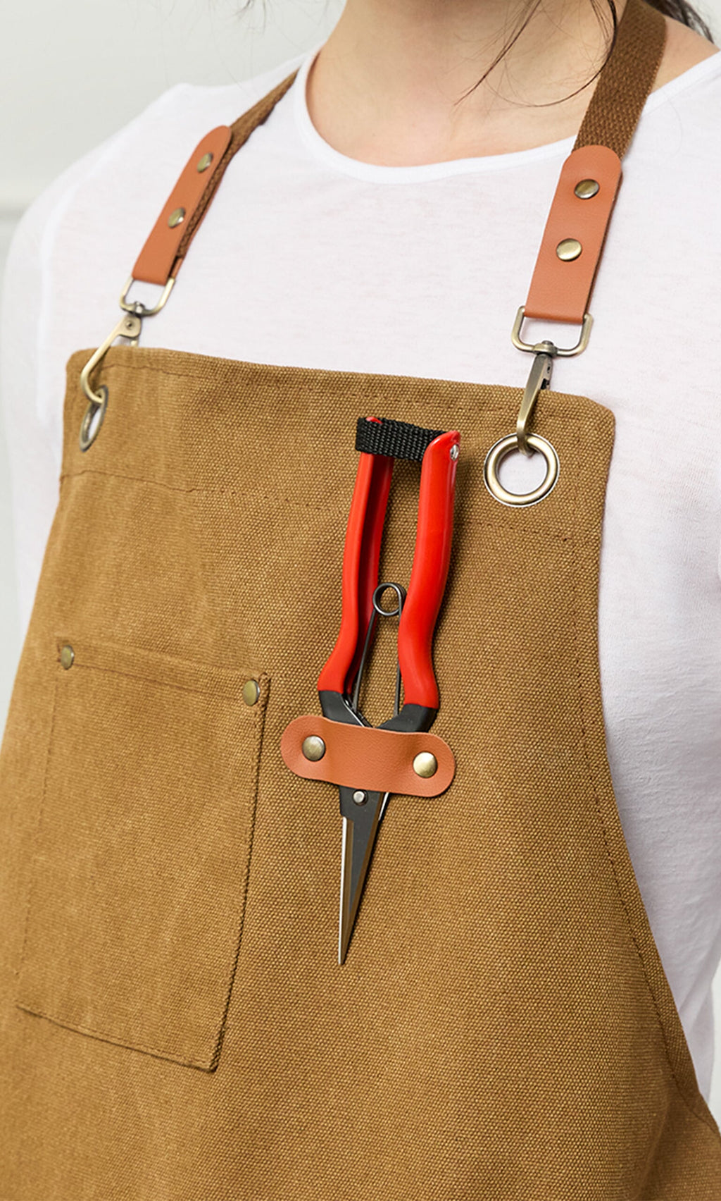 Plümo- Person wearing a brown apron with Red garden snips attached to the front chest strap.
