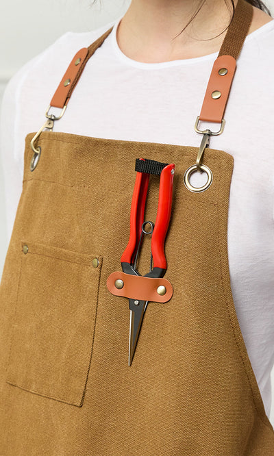 Plümo- Person wearing a brown apron with Red garden snips attached to the front chest strap.