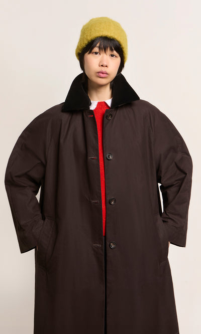 Plümo  Person in Danish design brown coat, Avo Wool Beanie, and red top stands against a plain background.