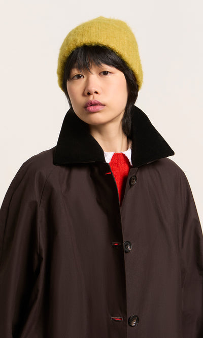 Plümo  Person in Danish design: wearing the Avo Wool Beanie yellow, brown coat with black collar, red top—facing camera.